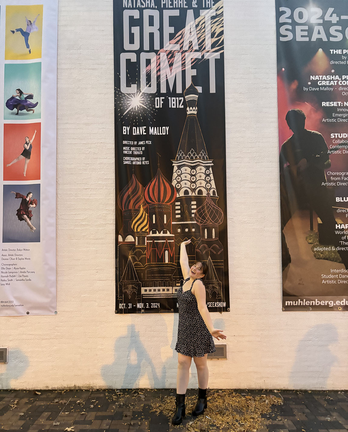 A college student stands in front of a banner advertising a performance of Natasha, Pierre & the Great Comet of 1812